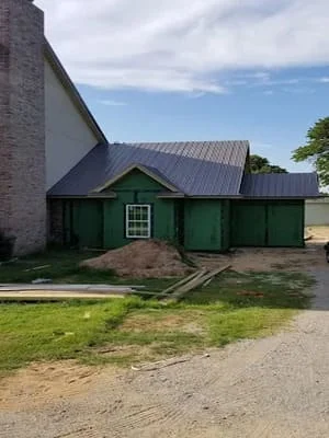 Standing seam metal roof installation on green agricultural building with pitched roof design