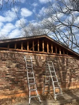 Brick gable with new wooden soffit and fascia installation, extension ladders positioned for access