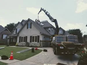 Crane truck positioned at residential home during roof replacement work