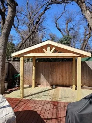 Timber pavilion with peaked roof, decorative gable detail, and composite deck among trees
