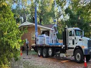 Roofing truck with hydraulic lift positioned at brick home for roof replacement project