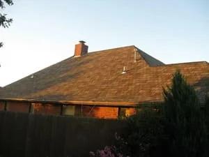Newly installed asphalt shingle roof with brick chimney and clean edge details