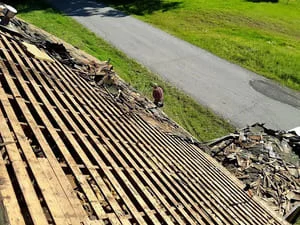 Corrugated metal roof panels installed with fasteners, adjacent graded landscape and asphalt driveway