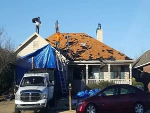 Residential roof replacement with new shingles being installed on home with blue tarping